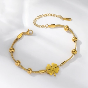 Detailed macro view of golden stainless steel snake chain bracelet with clover pendant