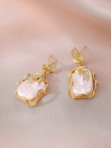 Detailed close-up of Baroque pearl earrings with golden leaves on soft silk fabric