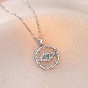 Silver evil eye heart necklace with green stone and pavé zircon on satin background