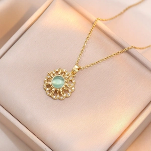 Detailed view of a gold sunburst necklace with a green gemstone and zircon in a gift box