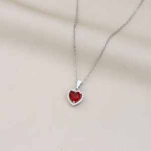 Primer plano de un collar de corazón plateado con gema roja sobre satén champán