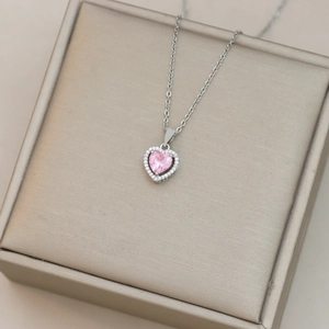 Vista macro de un collar de corazón rosa con halo de diamantes sobre un joyero elegante