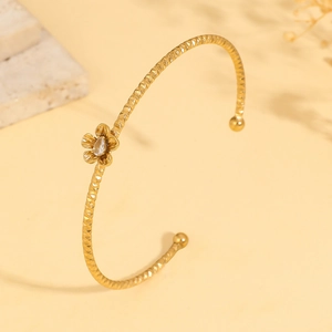 Detail of gold flower bangle with geometric texture and drop-shaped zircon stone