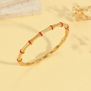 Detail van een gouden armband met bamboe-ontwerp en rode strassteentjes op een marmeren voet