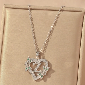 Macro detail of silver heart necklace pendant with letter Z and green gemstones