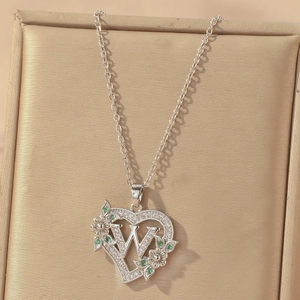 Macro view of silver heart pendant with letter W and green stones in gift box