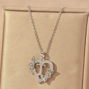 Close-up of heart-shaped letter T pendant with green zircon and floral details