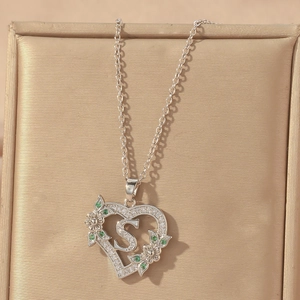 Detailed view of silver heart pendant with letter S and green zirconia stones