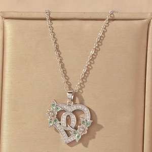 Detail of silver heart pendant featuring letter Q with green and white cubic zirconia
