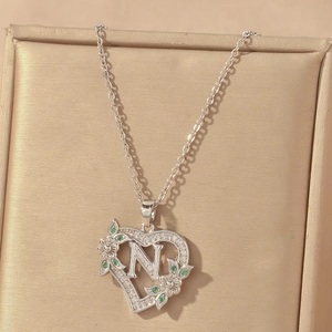Close-up of silver heart pendant with letter N, green gems and white zircons