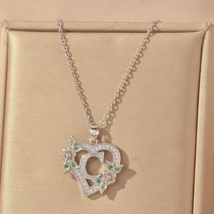 Detail of silver heart necklace with letter C, green stones and floral pattern