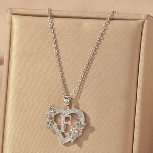 Detail of silver heart necklace with letter F, green stones and flower accents