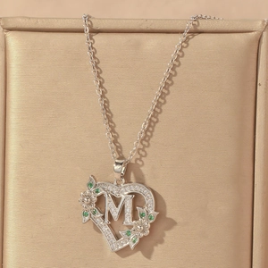 Macro detail of silver heart necklace with letter M and green floral accents
