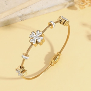 Dettaglio macro del bracciale rigido a spirale dorato con tre ciondoli a quadrifoglio