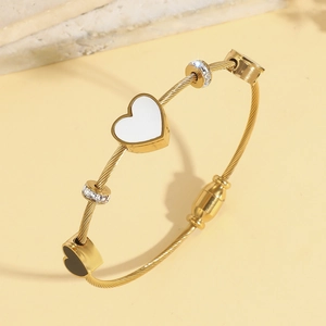 Vista dettagliata del bracciale dorato intrecciato con ciondolo a cuore bianco e perline