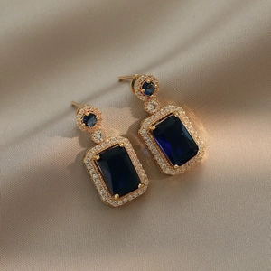 Detailed macro view of blue emerald-cut zircon earrings on champagne satin