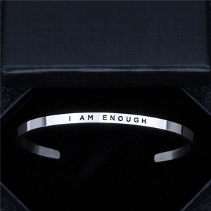 Macro view of silver stainless steel cuff bracelet engraved with I AM ENOUGH in a gift box
