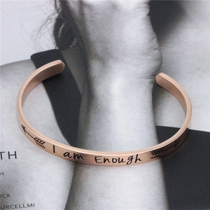 Dettaglio del bracciale rigido in oro rosa con incisione laser I am Enough e icone a freccia