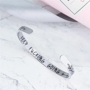 Bracciale argento lucido con incisione Keep Fucking Going su sfondo di marmo