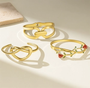 Detailed view of three gold knot heart and rose floral bangles on a stone background