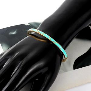 Dettaglio di un bracciale rigido dorato con smalto turchese su supporto mano nera