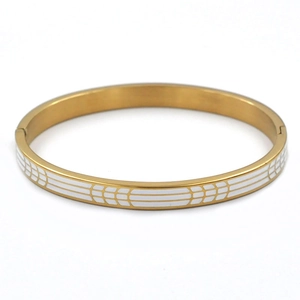 Vista detallada del brazalete de acero dorado con esmalte blanco y diseño de líneas geométricas