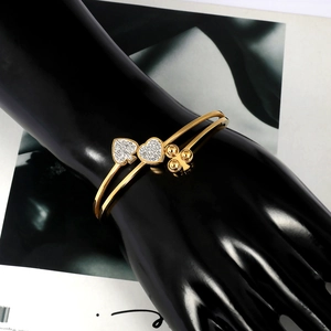 Dettaglio del bracciale aperto dorato a doppio strato con ciondoli a cuore e picche in diamanti