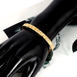 Close-up of gold titanium steel rivet bangle with pyramid texture on a black hand model
