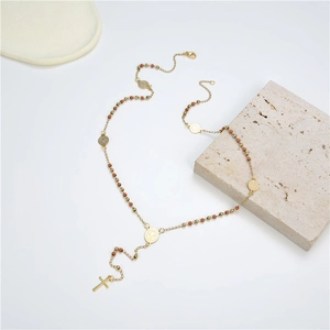 Collier croix doré avec perles colorées et médailles rondes sur un support en pierre