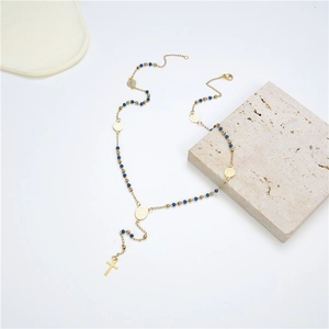 Détail d'un pendentif croix dorée avec perles bleues sur un support en pierre texturée