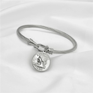Dettaglio del bracciale a cavo argentato con ciondolo a moneta vintage su seta bianca pura