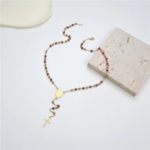 Detail of gold beaded cross necklace with red beads and religious medallion charm