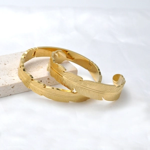 Bracciali a piuma dorati con trame dettagliate su sfondo di marmo bianco