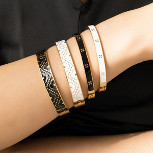 Detailed close-up of four gold stainless steel bangles with black and white enamel flowers