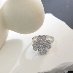 Polished silver clover ring with sparkling zircon stones on a white stone background