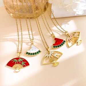 Gold bamboo leaf fan and watermelon pendant necklaces set on marble surface