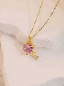 Detailed view of a gold heart-shaped pink gemstone key pendant necklace on a stone display