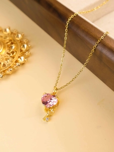Detail of pink heart gemstone and gold key pendant with crystal on a delicate chain