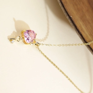 Golden heart necklace with pink crystal and key pendant on a minimalist cream card