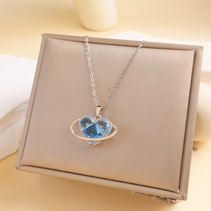 Saturn-shaped heart pendant necklace with blue gemstone and silver chain on jewelry box