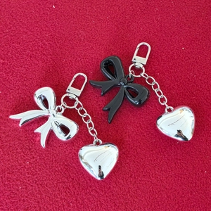 Polished silver metal bow and heart pendant keychain on red fabric background