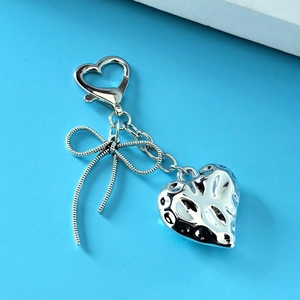 Macro detail of silver acrylic heart and metal bow keychain on a light blue background