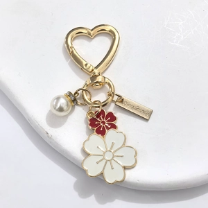Detail of a handmade heart keychain with enamel flowers, pearls, and gold finish