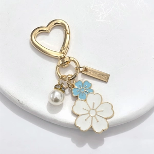 Detail of flower keychain with heart clasp, faux pearl, and handmade tag on white stand