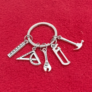 Détail d'un porte-clés à outils argentés comprenant mini scie, marteau, règle et pince