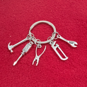 Porte-clés en métal argenté avec mini breloques d'outils DIY sur fond de velours rouge