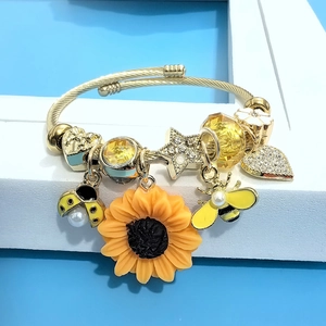 Detail of gold twisted bangle with enamel sunflower, bee charms and faceted yellow beads