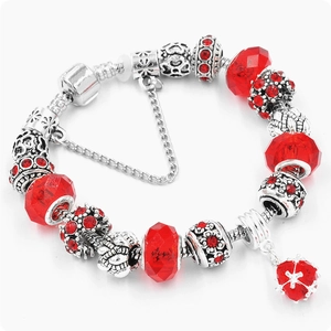 Macro shot of silver charm bracelet featuring ruby red glass beads and heart pendant