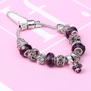 Macro view of purple faceted crystal beads and silver flower charms on a snake chain bracelet