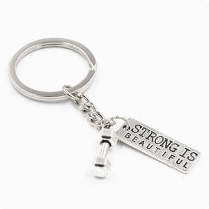 Silver fitness dumbbell keychain with Strong Is Beautiful tag on white background